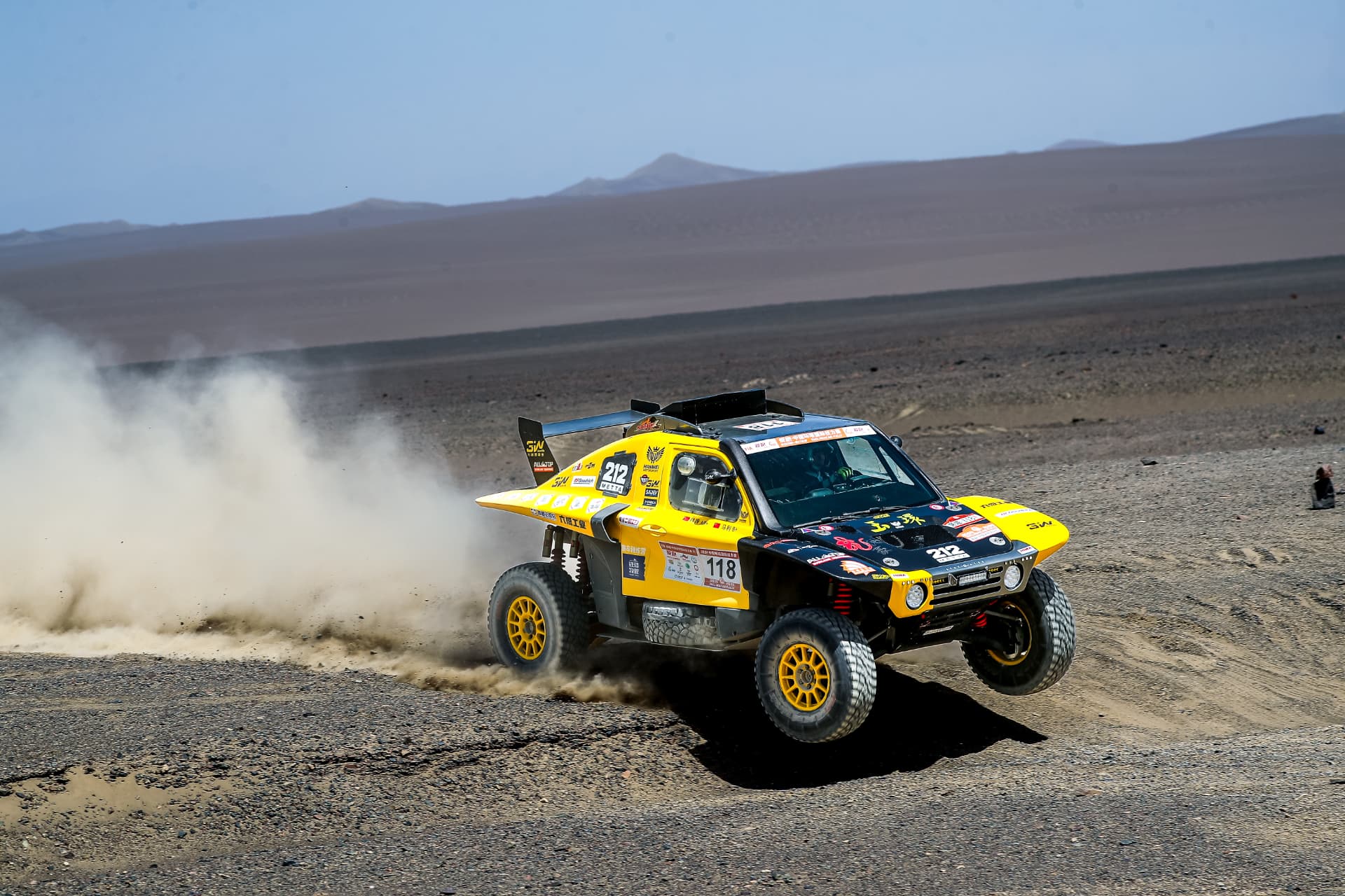 The HWM rally car number 118 airborne over a stony ridge in Gobi desert terrain, trailing a plume of dust