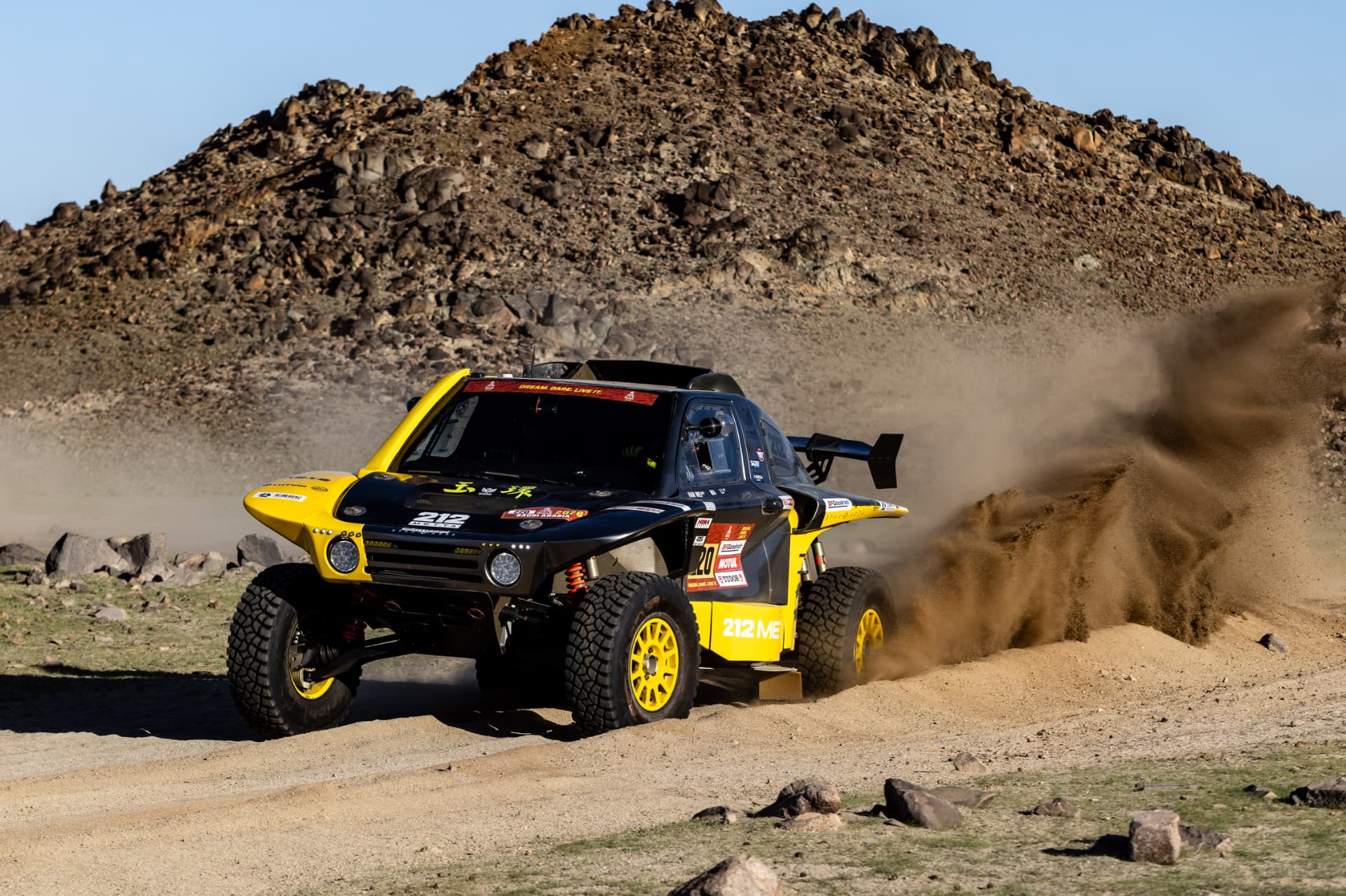 HWM T1+ race car number 220 on a desert stage beside a rocky hillside